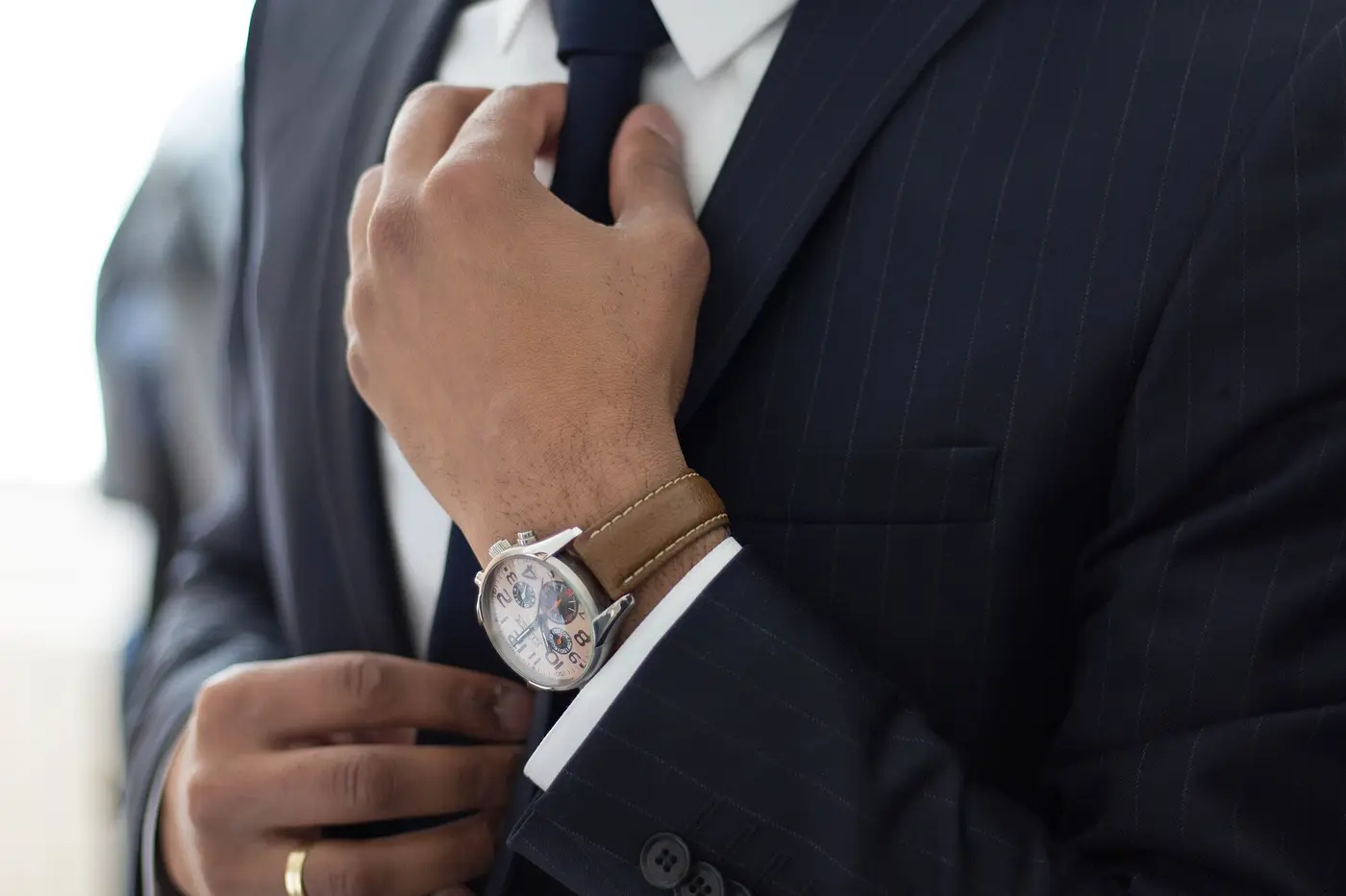 Homme en costume qui ajuste sa cravate, montre au poignet