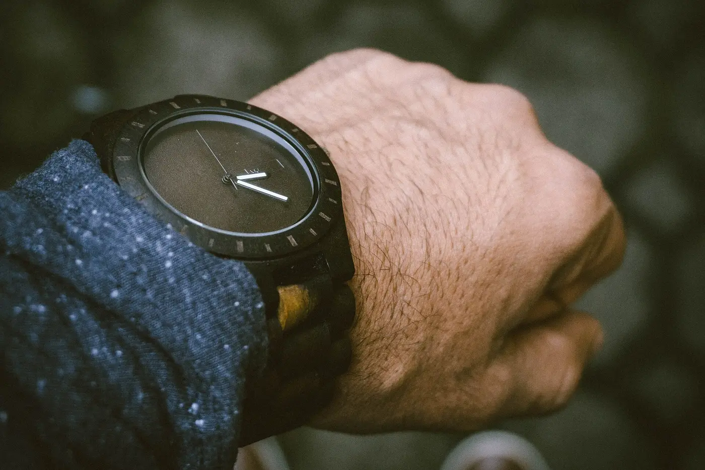 Montre noire au poignet d'une veste en tweed